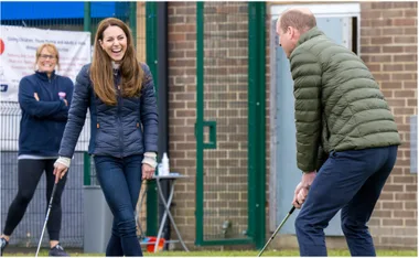 A woman and man laugh while playing golf, a bystander watches in the background.