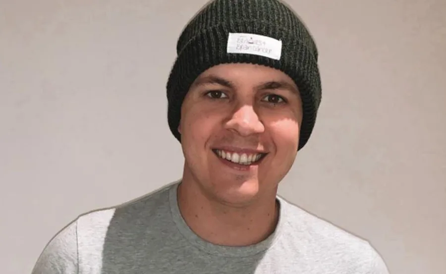 Smiling person in a black beanie and gray shirt against a plain background.