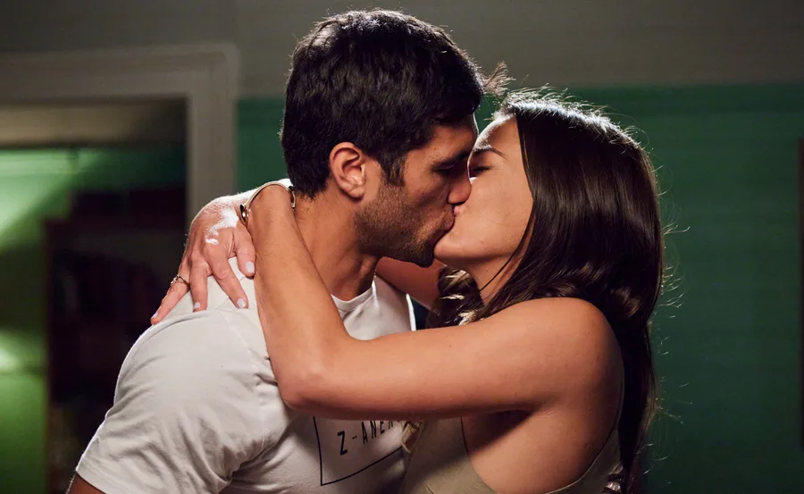 A couple shares a passionate kiss in a dimly lit room.