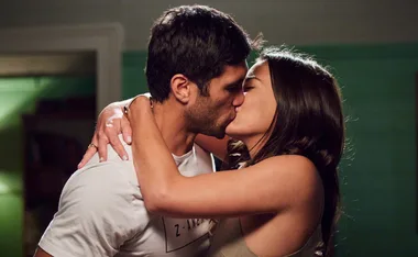 A couple shares a passionate kiss in a dimly lit room.