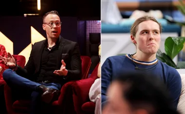 Two men sit indoors; one in glasses gesturing, the other in a blue sweater, looking thoughtful.