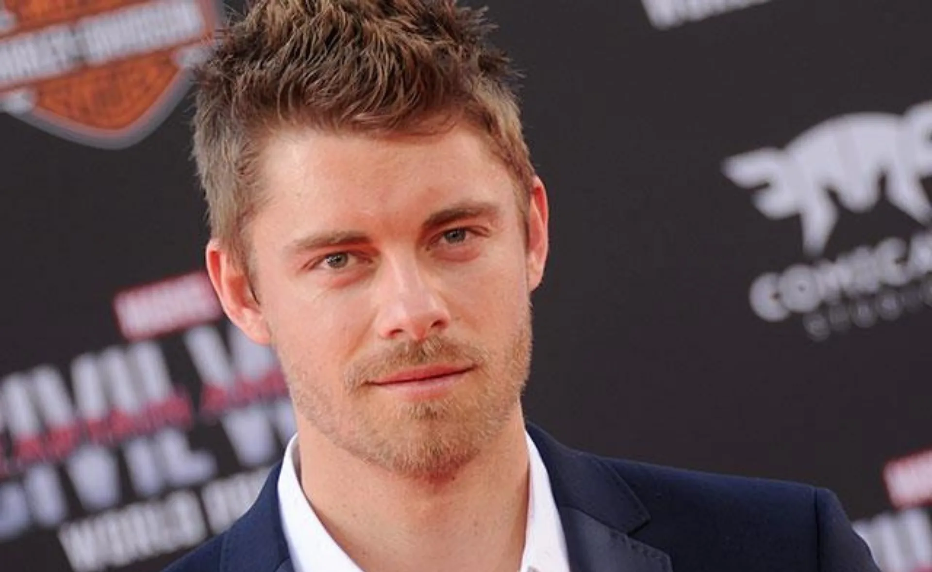 A man with short hair and a beard in a suit at a red carpet event.