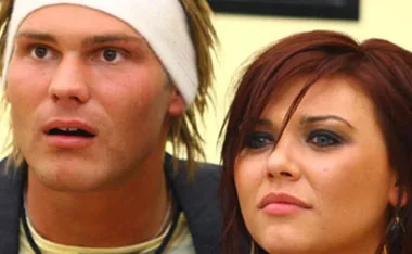 Two people looking surprised; one wears a headband, the other has dark hair and makeup.