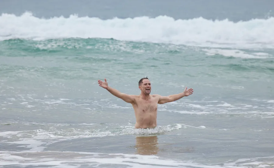 Man standing joyfully in ocean waves with arms wide open, smiling.