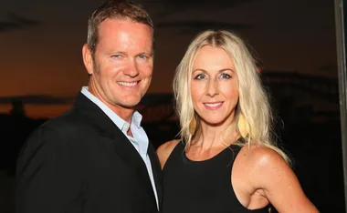 A man and woman smiling at the camera, standing close together with a sunset background.