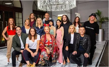 Group of 15 people posing indoors, some seated, others standing, with a modern decor background.