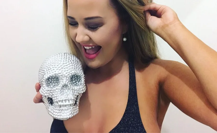 Woman smiling, holding a crystal-studded skull, wearing a dark top.