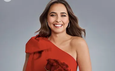 A woman in a red dress smiles against a gray background.