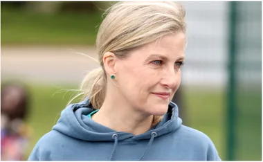 A woman in a blue hoodie looking to the side, outside on a blurred green background.