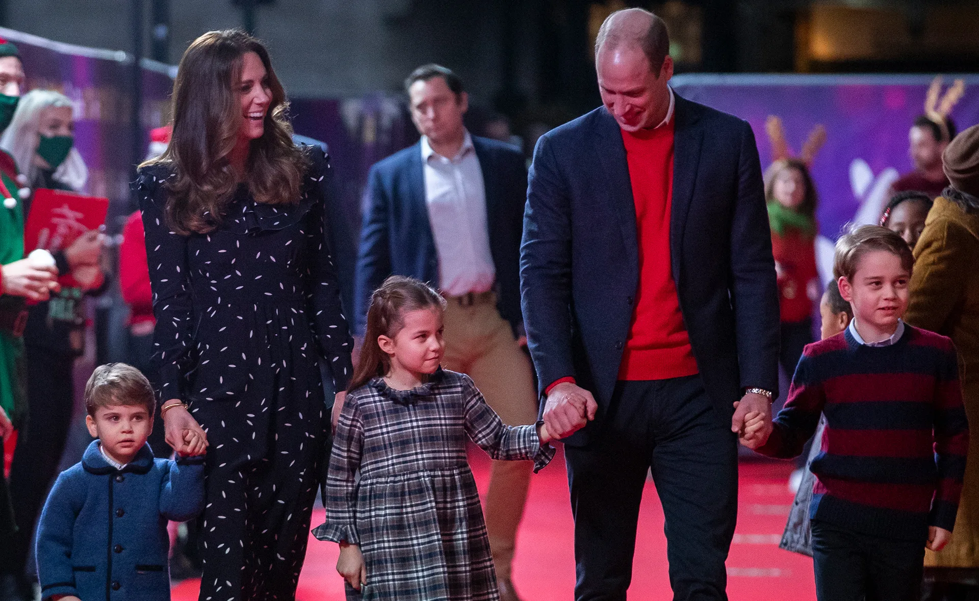 Kate and William with their children on a red carpet at a festive event, surrounded by other people.
