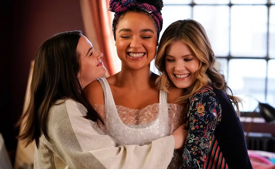Three women sharing a joyful hug, with one smiling widely at the center.