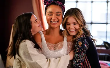 Three women sharing a joyful hug, with one smiling widely at the center.