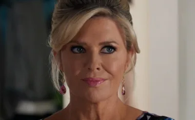 Woman with blonde hair up, pink lipstick, earrings, looking sideways.