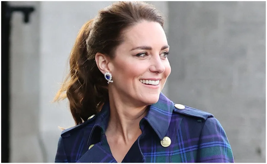 A woman smiling, wearing a plaid coat and gemstone earrings outdoors.