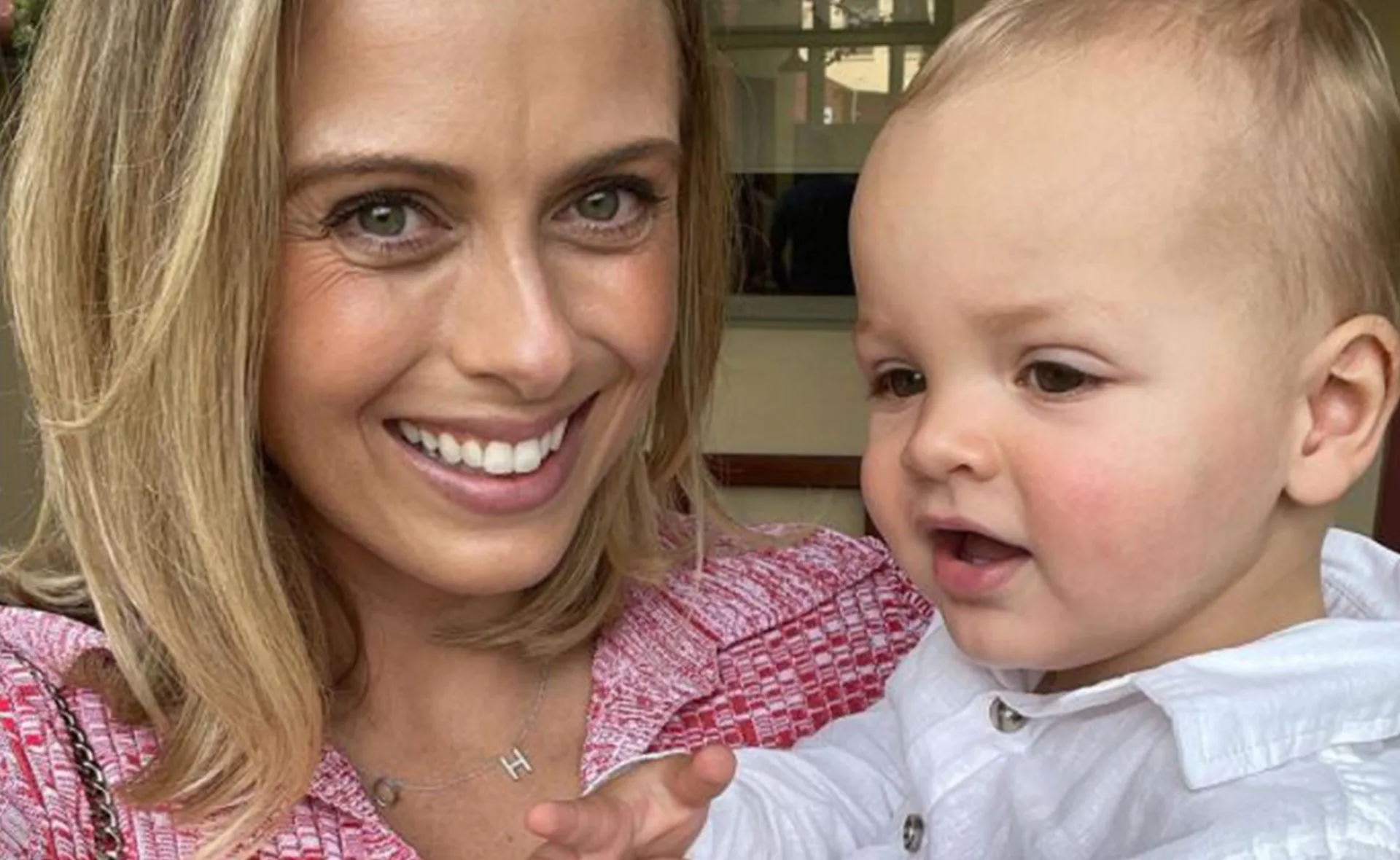 A woman in a pink outfit smiles while holding a baby in a white shirt.