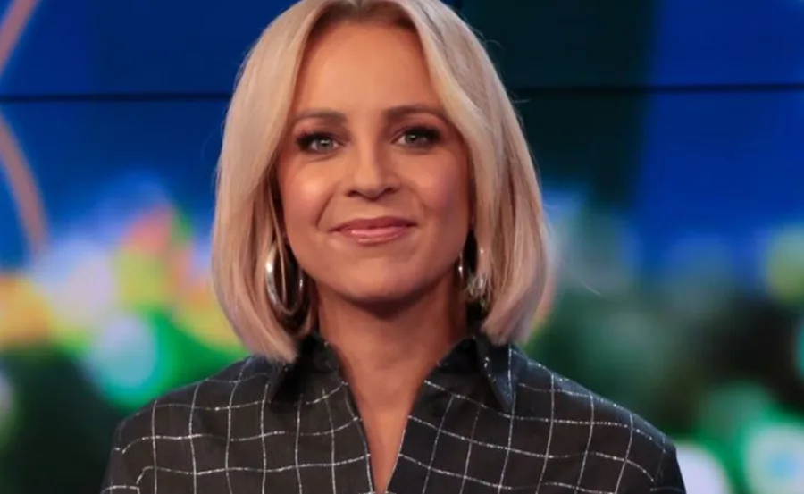 A person with blonde hair wearing a checkered shirt and hoop earrings, smiling at the camera.