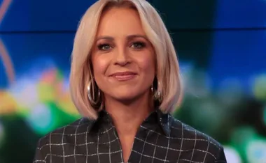 A person with blonde hair wearing a checkered shirt and hoop earrings, smiling at the camera.