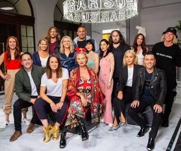 Group photo of "The Celebrity Apprentice" cast posing in luxurious indoor setting, including men and women in vibrant outfits.