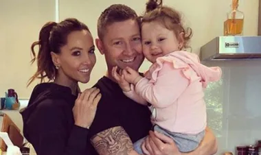 A smiling couple holds their young child in a kitchen setting, showing warmth and happiness.