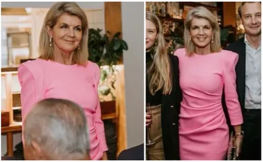 A woman in a stylish pink dress with shoulder pads, standing indoors and smiling with others.