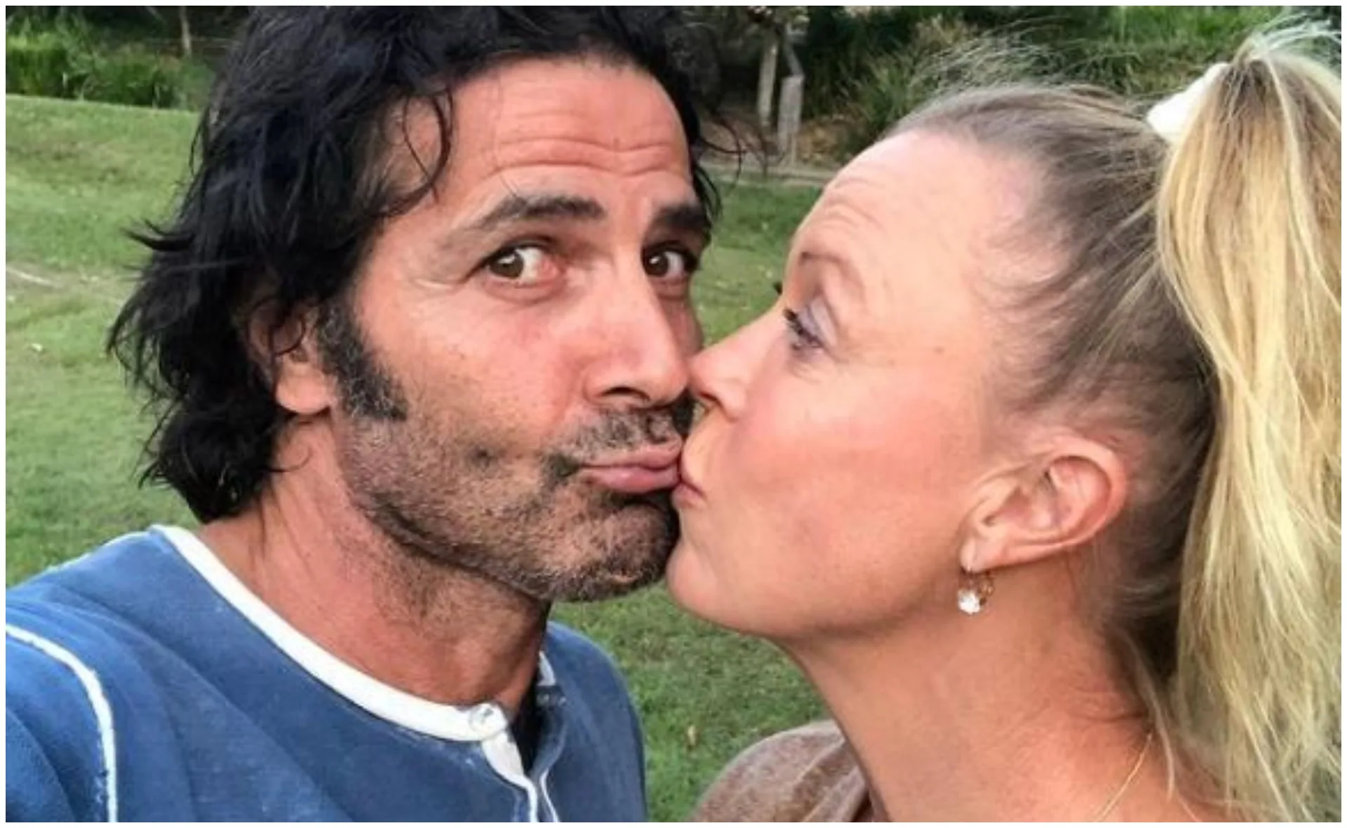 A woman and man kissing outdoors, with greenery in the background.