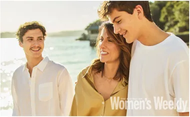A woman and two young men smiling by the seaside, featured on a magazine cover.