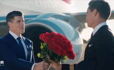 Two men exchange a bouquet of red roses in front of an airplane on the tarmac.