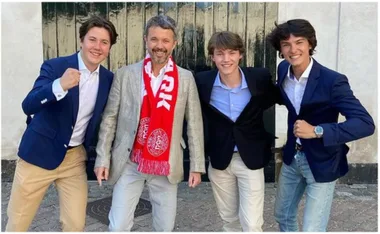 A group of four people smiling at the camera; one wears a red scarf with white text.