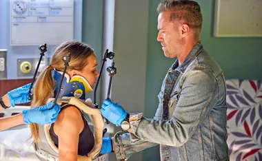 Man in denim helps woman in medical halo brace in a hospital setting.