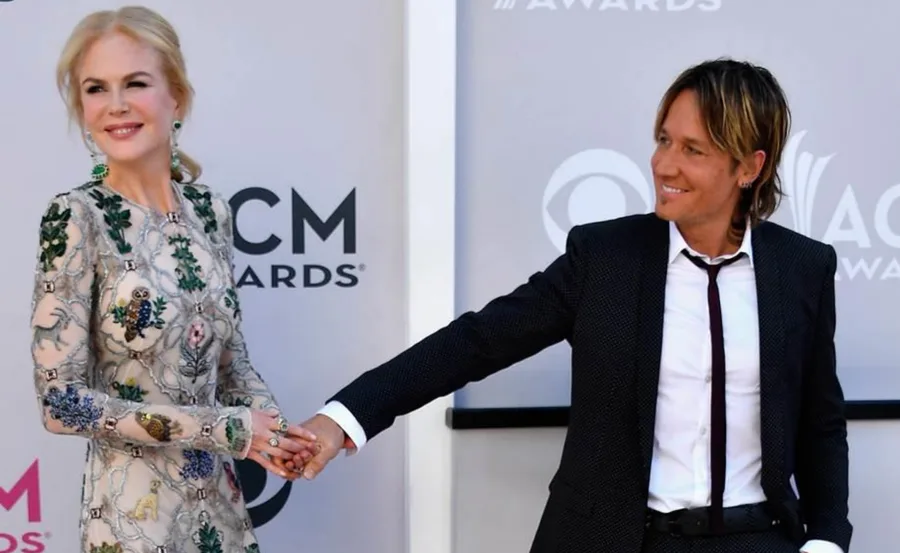 Couple holding hands, posing on the red carpet at ACM Awards; woman in an embroidered dress, man in a suit.