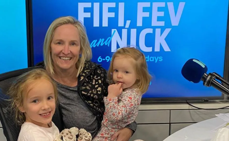 Woman with two children in a radio studio with "Fifi, Fev and Nick" sign in background.