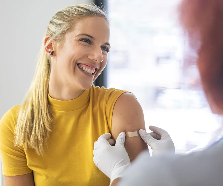 Smiling woman in yellow shirt receives a flu shot with a bandage on her arm in a healthcare setting.