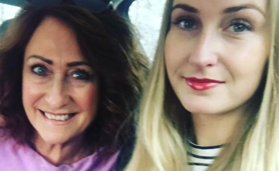 Two women taking a selfie in a car, both smiling with one having dark hair and the other blonde.