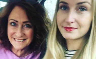 Two women taking a selfie in a car, both smiling with one having dark hair and the other blonde.