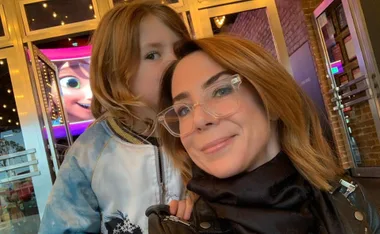 Woman in glasses and child in a movie theater lobby; Frozen character visible on screen in background.