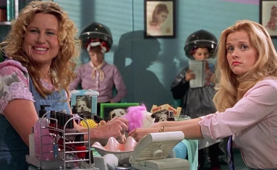Women in a salon; one smiling, one concerned; others under hair dryers.