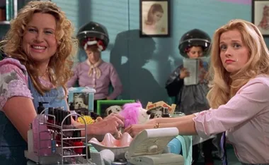Women in a salon; one smiling, one concerned; others under hair dryers.