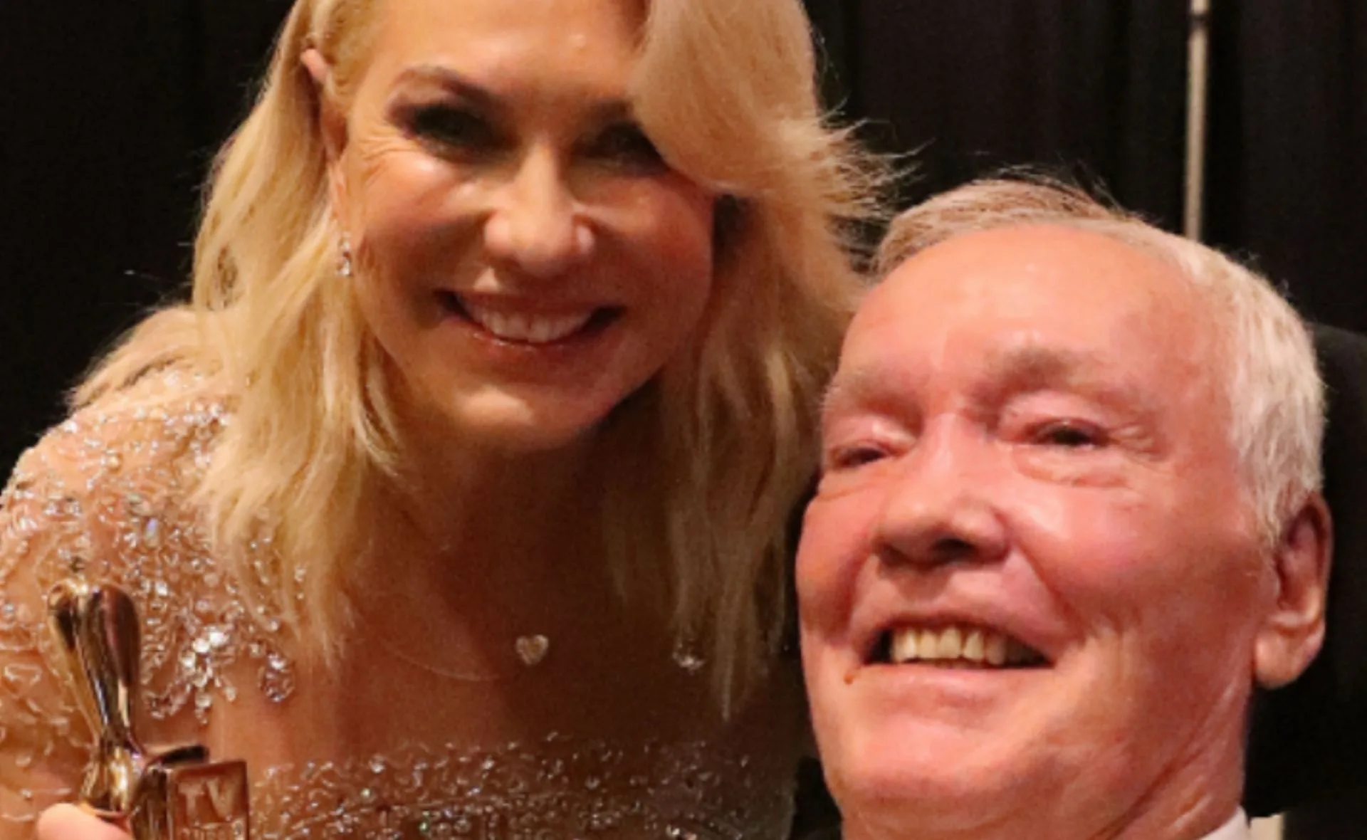 Woman in embellished dress smiles with a man. They both look happy and are in a close-up shot.