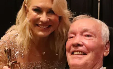 Woman in embellished dress smiles with a man. They both look happy and are in a close-up shot.