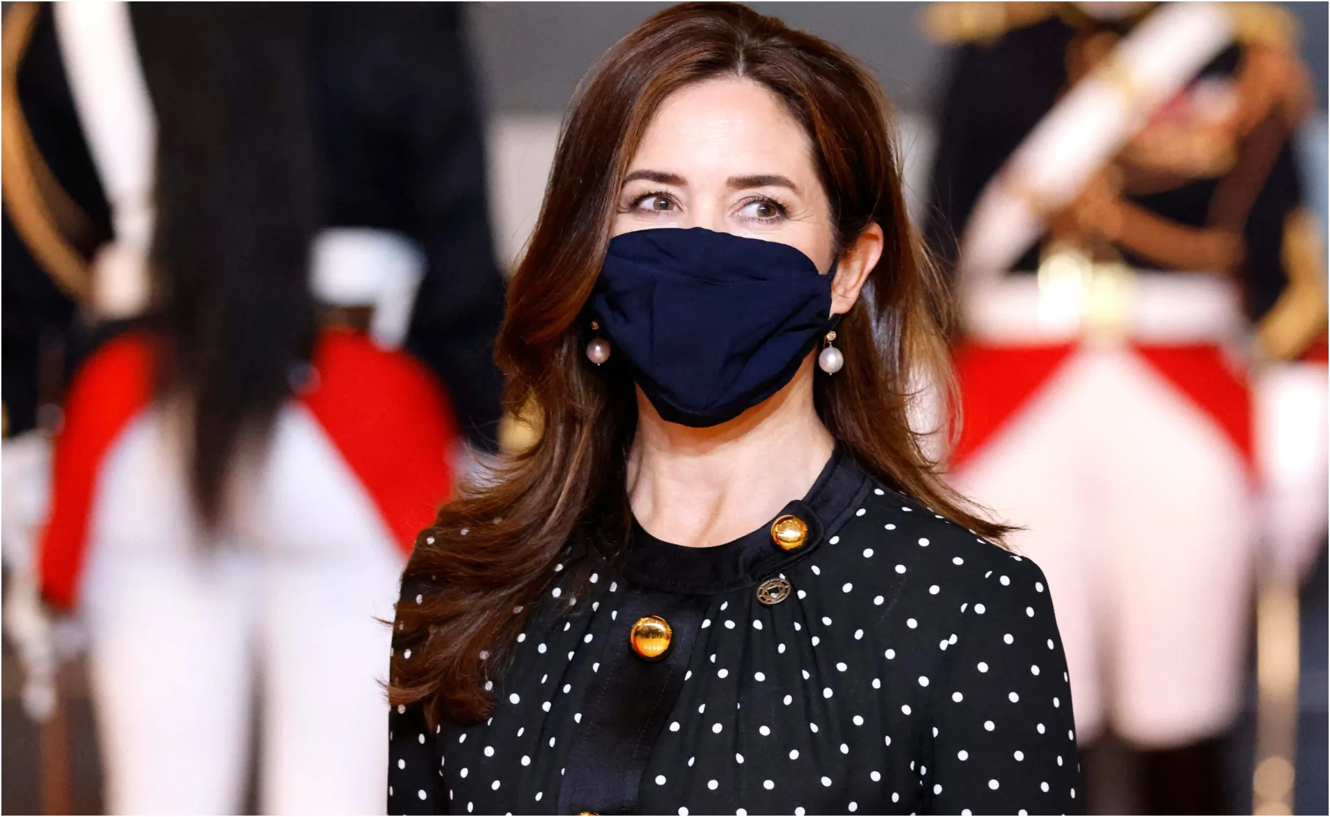 Princess Mary wearing a black mask and polka dot dress, pearl earrings, background with formal guards.
