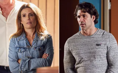 A woman in a denim jacket and a man in a grey sweater stand apart, both with serious expressions indoors.