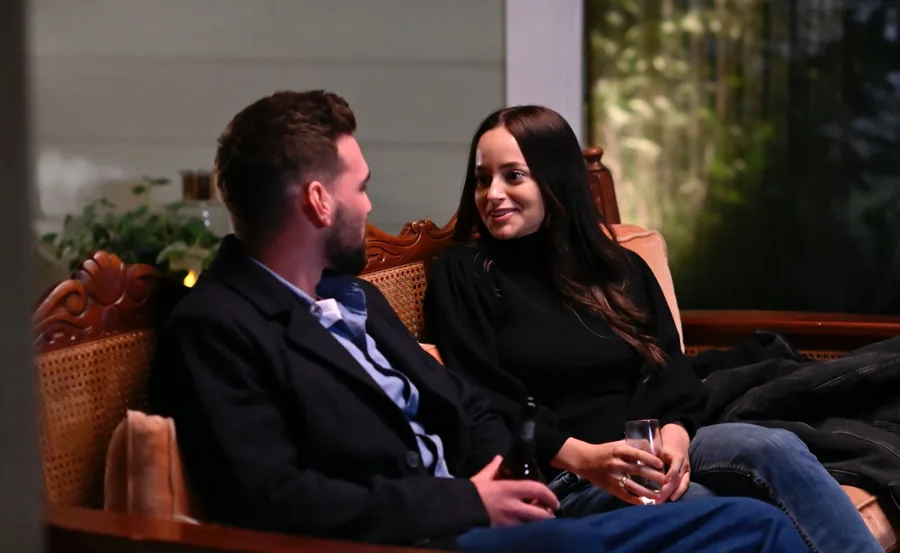Couple sitting on a wooden bench, smiling and talking, each holding a drink.