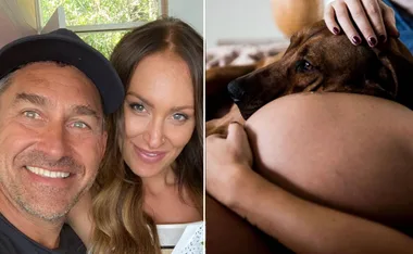 Couple smiling together; dog resting on pregnant belly.