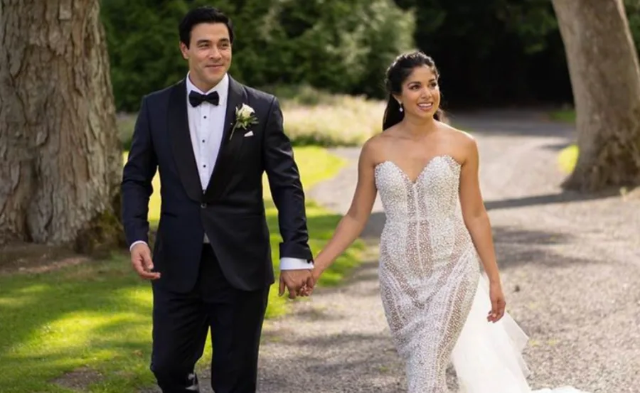 A couple walking hand in hand on a garden path; the woman in a strapless wedding dress, the man in a tuxedo.