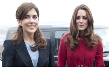 Two women with long brown hair, one in a black coat and one in a red coat, standing outdoors near a vehicle.
