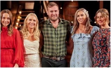 A group of five people standing together in a well-lit room, with candles visible in the background.