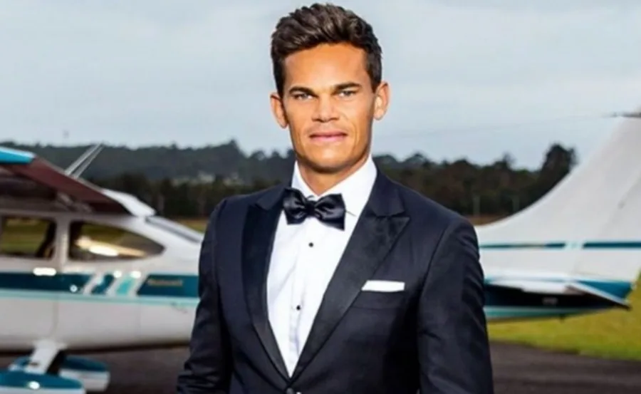 Man in a tuxedo standing in front of a small airplane on a runway.