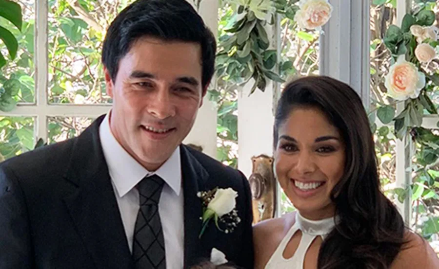 "Couple smiling in formal attire in front of floral backdrop, celebrating a special occasion."