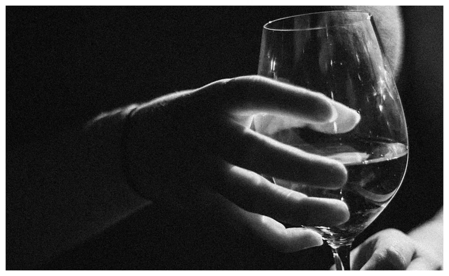 A hand holding a wine glass in a dark setting, highlighting themes of addiction and alcohol use.