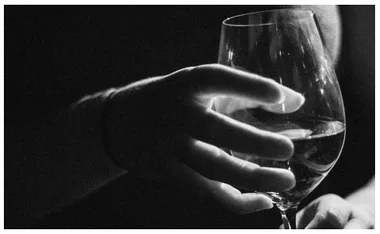 A hand holding a wine glass in a dark setting, highlighting themes of addiction and alcohol use.